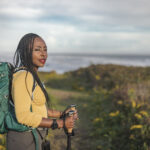 A frustrated African American woman with hiking poles on a hiking trail and showing a little teeth sucking rage.