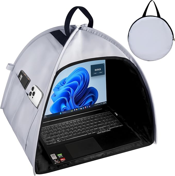 Protective laptop tent in use outdoors, helping reduce sun glare. A smartphone and power bank are stored in side pockets. A Windows laptop is visible inside. Tent folds into a round gray carrying case.